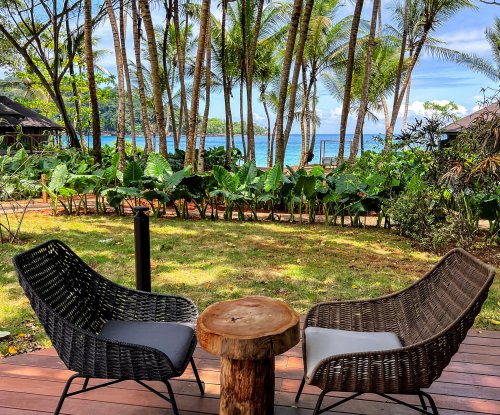 Duas cadeiras e uma mesa em uma varanda com vegetação exuberante ao fundo no Bom Bom Resort.