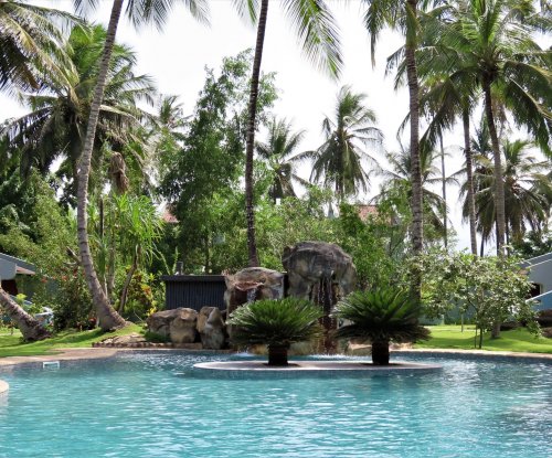 Swimming pool and shady tables at Omali, surrounded by palm trees and lush greenery.