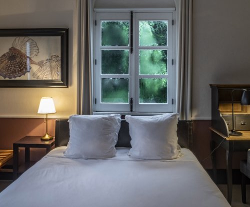Cozy bedroom at Roça Sundy featuring a bed, a desk, a window with greenery view, and soft lighting