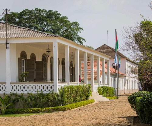 Exterior view of Roça Sundy entrance with white pillars, arched windows, and lush greenery