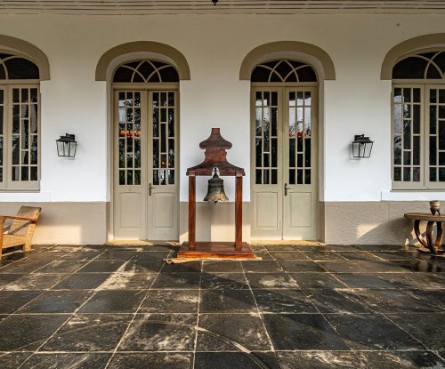 Entrada da Roça Sundy com portas de estilo colonial, um sino e cadeiras de madeira na varanda