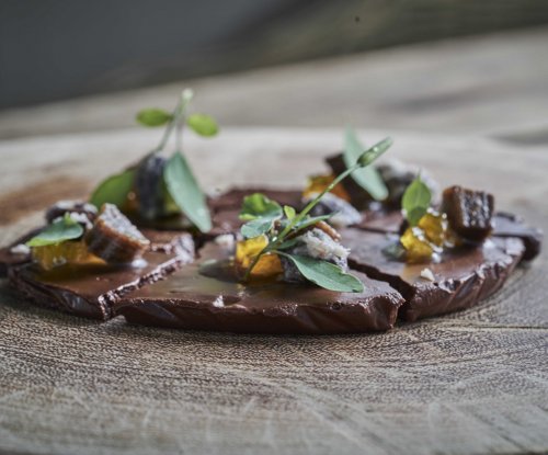 Close-up of an elegant chocolate dessert garnished with herbs and fruits, served on a wooden plate at OKA Sundy restaurant