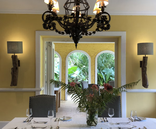 Elegant dining room at Belo Monte with chandelier, white tablecloth and garden views through arched doors.