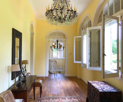 Elegant corridor at Belo Monte with chandelier, wooden floor and patterned rug, windows open to the gardens.