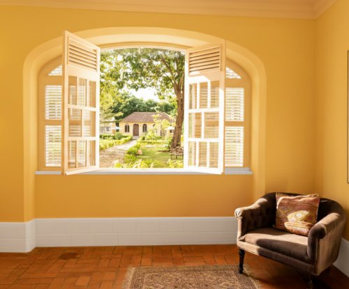 Sunlit window at Belo Monte opening to the courtyard gardens with yellow buildings and a cosy armchair inside.