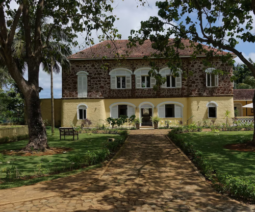 Casa principal do Belo Monte entre árvores, fachada em pedra e amarelo com janelas em arco e caminho pelo jardim.