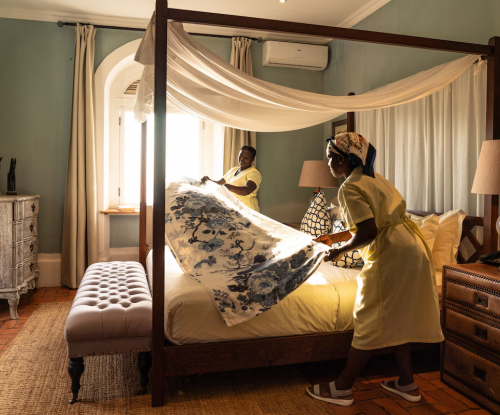 Housekeeping preparing a four-poster bed with floral cover in the Panoramic Suite at Belo Monte, soft morning light.