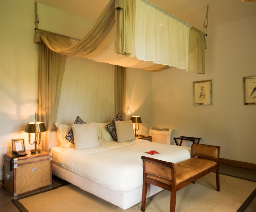 Panoramic Suite bedroom with canopy bed, warm lamps and leather bench, framed bird prints on the wall.
