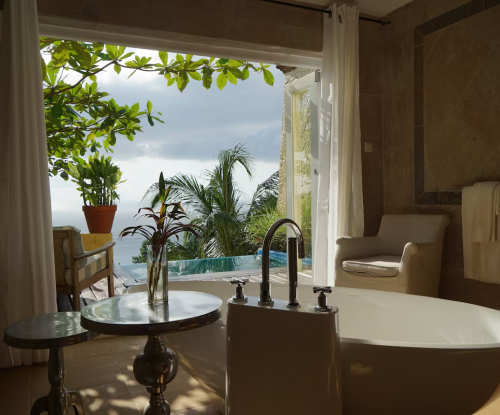 Panoramic Suite bathroom at Belo Monte with freestanding tub, doors to terrace and plunge pool, ocean view through tropical leaves.