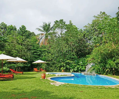 Garden pool at Belo Monte with lawn loungers, umbrellas and a rock waterfall surrounded by tropical greenery.