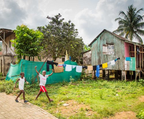Two children laughing at the camera, with local huts and laundry hanging to dry in the background.