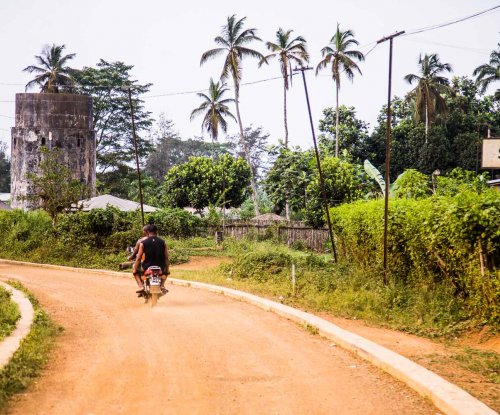 Dois locais a andar de mota numa estrada de terra em Sundy, Ilha do Príncipe.