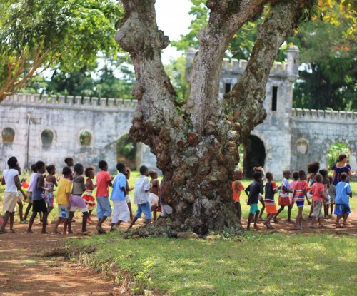 Um grupo de crianças vestidas de forma colorida atrás de uma árvore em frente à Roca Sundy, Ilha do Príncipe.