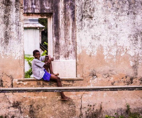 Child in purple shorts and a magenta T-shirt sitting on an outdoor window bench