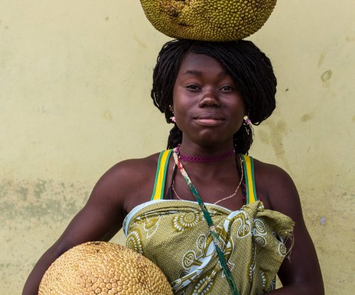 Portrait of a smiling woman balancing a large fruit on her head