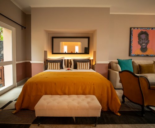 Belo Monte bedroom with an ochre bedspread, framed portrait and garden view through tall windows