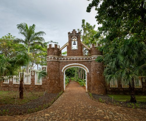 Portão fortificado em pedra e campanário ladeados por palmeiras e jardins tropicais no Belo Monte