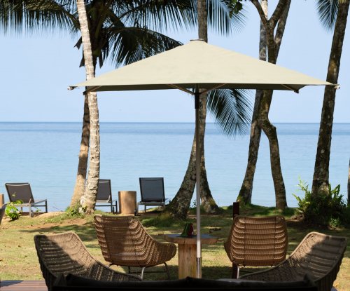 Wicker chairs and parasol on the Bom Bom Beach Club terrace, with palm trees and the ocean in the background, Príncipe Island