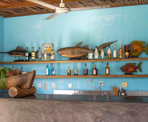 Bar do Omali com paredes azuis, esculturas de peixes em madeira e garrafas em prateleiras abertas, Ilha de São Tomé