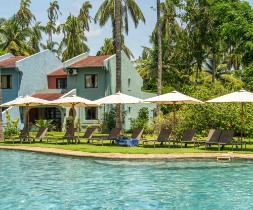 Espreguiçadeiras e chapéus de sol junto à piscina do Omali, com edifícios em tons pastel e palmeiras ao fundo, Ilha de São Tomé
