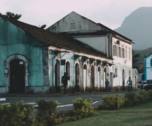 Edifícios coloniais coloridos e igreja azul com pico rochoso ao fundo em Santo António, Ilha do Príncipe
