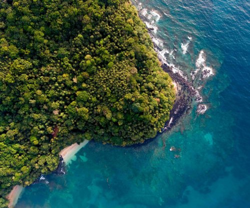 Vista aérea de um promontório rochoso coberto de floresta com pequena praia isolada, Ilha do Príncipe