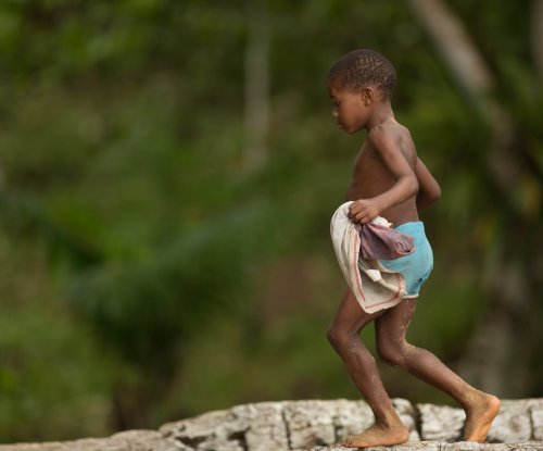 Criança a caminhar descalça sobre um tronco de árvore junto à praia, Ilha do Príncipe