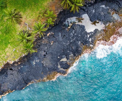 Aerial view of dark volcanic rocks meeting the turquoise ocean at Boca do Inferno, São Tomé Island