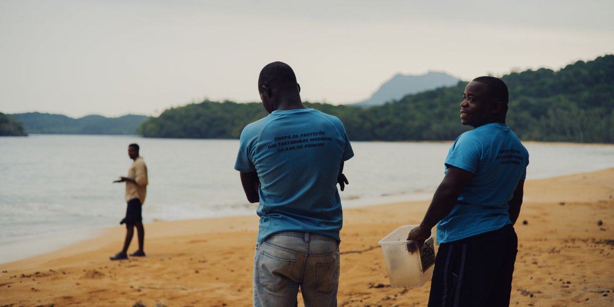 Three locals on Principe Island beach, one holding a plastic container.
