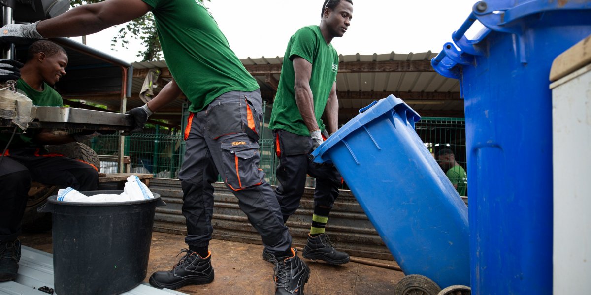 Three workers in green T-shirts recycling with blue bins on Príncipe Island.