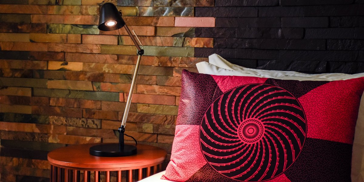 Cama com almofada vermelha estampada e parede de pedra no Omali.