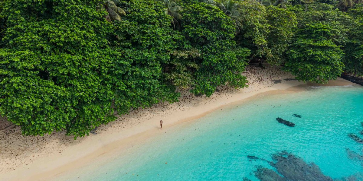 Vista aérea de praia isolada com rochas vulcânicas, areia dourada e águas turquesa cristalinas, Ilha do Príncipe