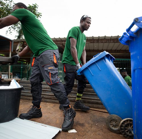 Three workers in green T-shirts recycling with blue bins on Príncipe Island.