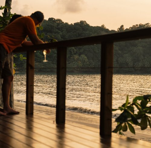 Um homem segurando uma bebida na praia durante o pôr do sol no Bom Bom Beach Resort.