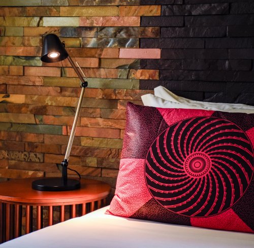 Cama com almofada vermelha estampada e parede de pedra no Omali.