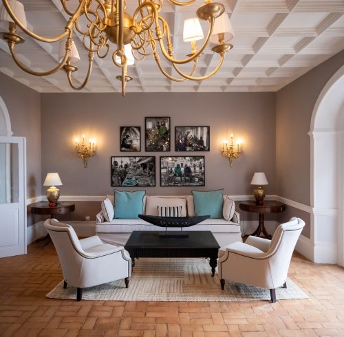Sala de estar do Belo Monte com candelabro dourado, fotografias da ilha emolduradas e vista para o mar através das portas em arco