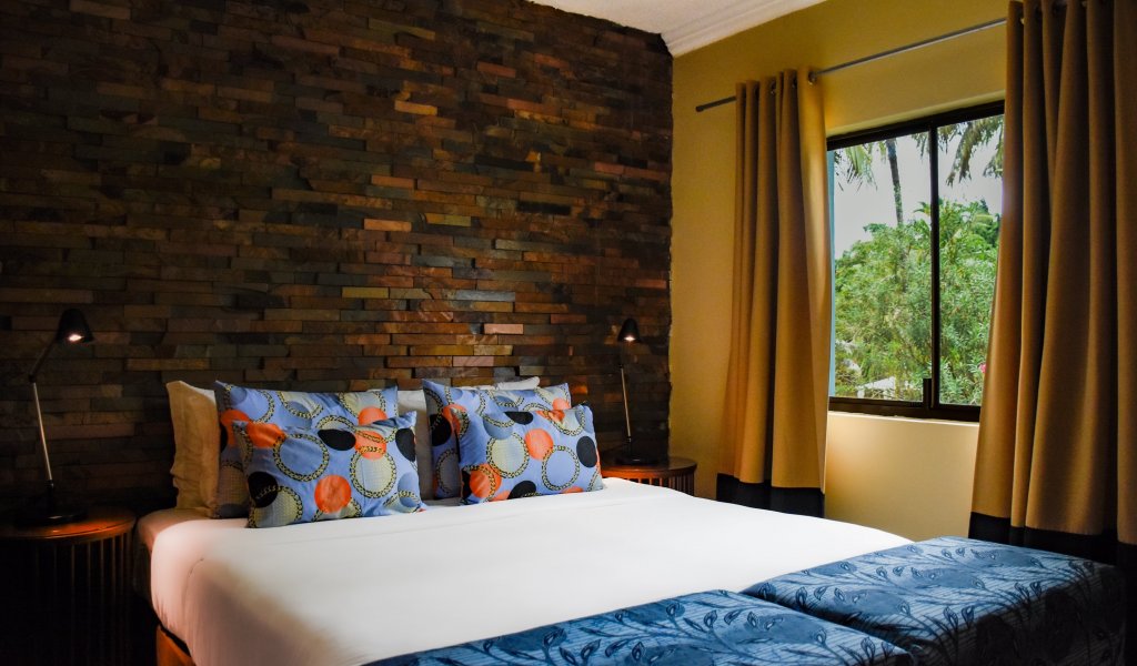 Bedroom with blue ottomans, stone wall, and a woven light fixture at Omali.