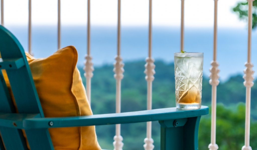 Glass of a refreshing drink on a balcony with ocean and forest views at Roça Sundy