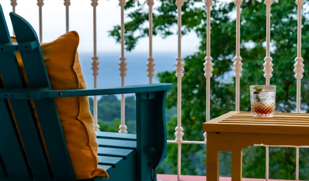 Glass of a refreshing drink on a balcony with ocean and forest views at Roça Sundy