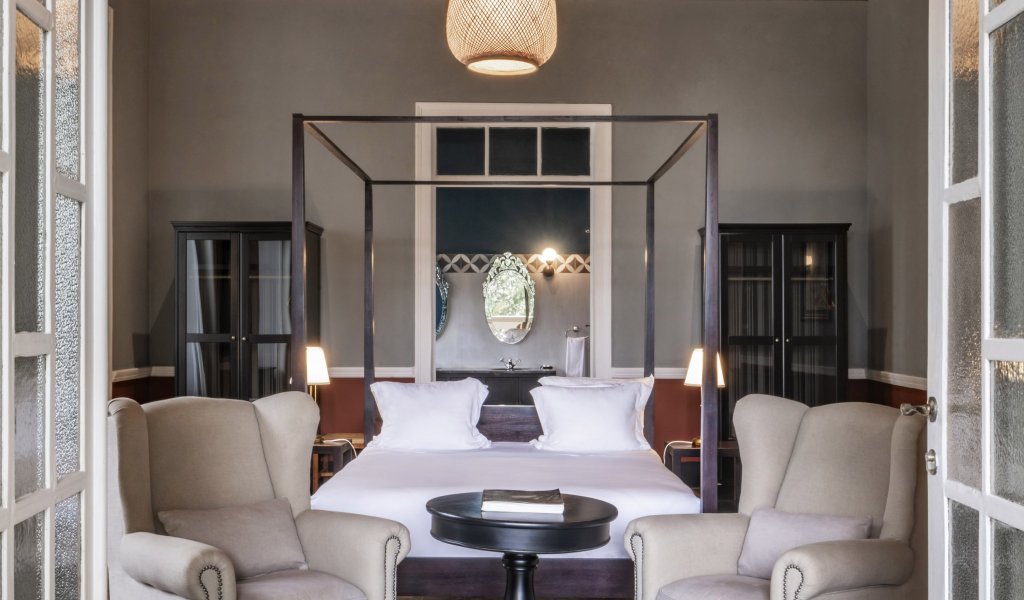 Spacious suite at Eclipse House in Roça Sundy with a four-poster bed, armchairs, and wooden ceiling
