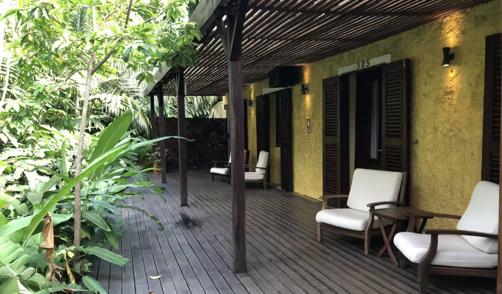 Shaded veranda outside the Garden Rooms, wooden deck seating amid lush tropical plants, calm retreat setting.