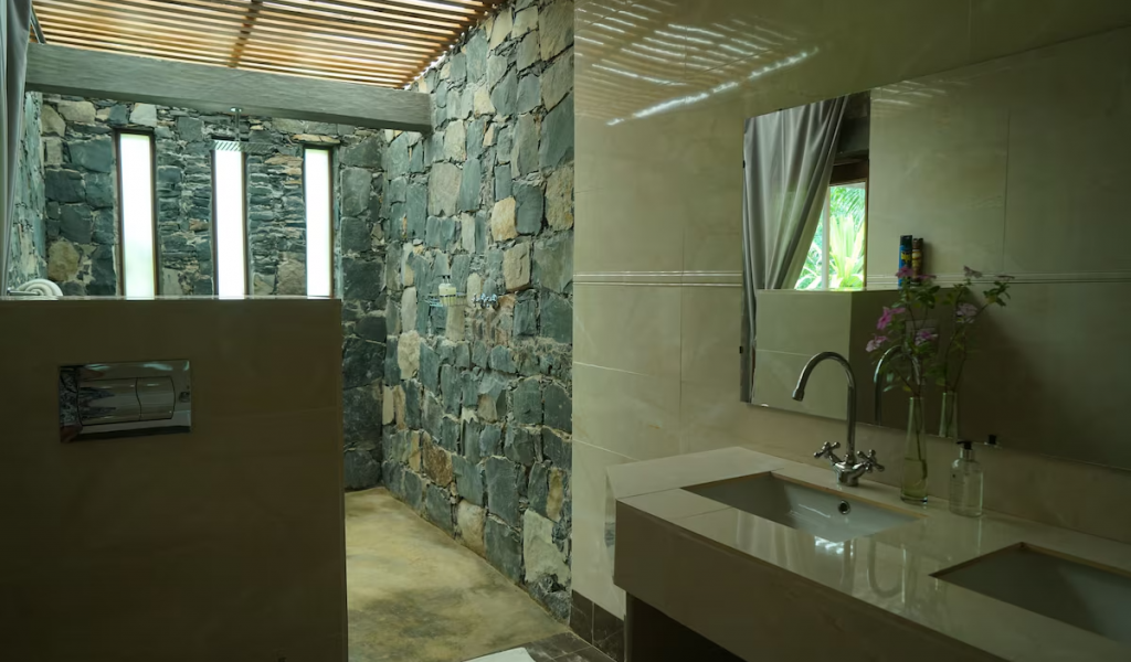 Panoramic Suite bathroom with stone walk-in shower, slatted roof light and double vanity facing a garden window.
