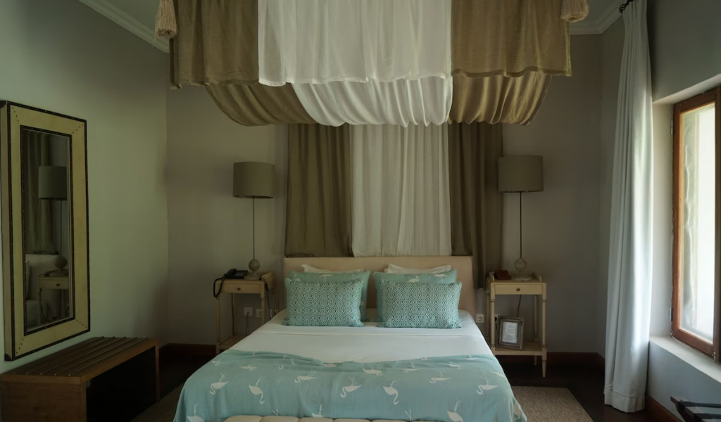 Suite at Belo Monte with draped canopy, soft blue textiles and a tufted bench, natural light from the window.