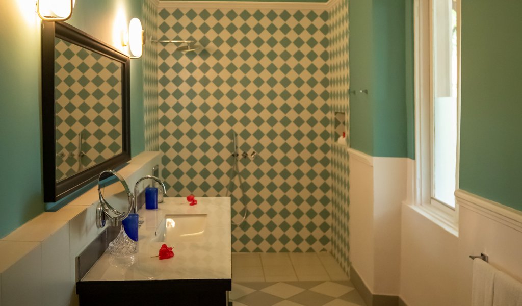 Casa de banho do Belo Monte com azulejos axadrezados verdes e brancos, bancada em mármore e chuveiro de acesso aberto