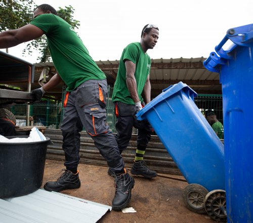 Three workers in green T-shirts recycling with blue bins on Príncipe Island.