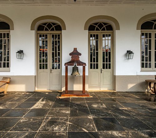 Entrada da Roça Sundy com portas de estilo colonial, um sino e cadeiras de madeira na varanda