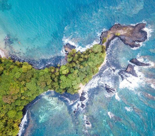Aerial view of Príncipe Island with crystal-clear turquoise water and lush rainforest vegetation.